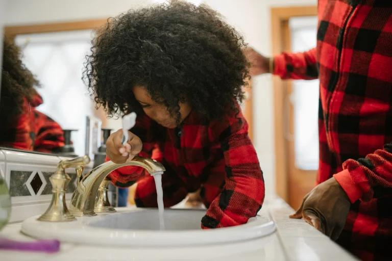 A father helps his daughter brush her teeth at the bathroom sink, highlighting family routines.