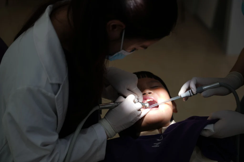 A young child undergoing a dental procedure in a clinic, with a dentist attending.
