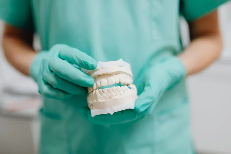 Dentist holding a dental cast with green gloves, representing dental care and prosthetics.