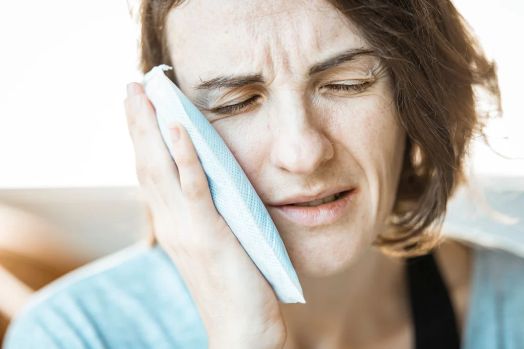 A woman in discomfort applying a cold compress to her cheek for relief from toothache pain.