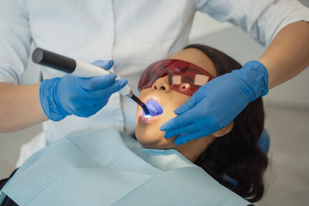 Dentist performing dental treatment using curing light on patient wearing protective eyewear.