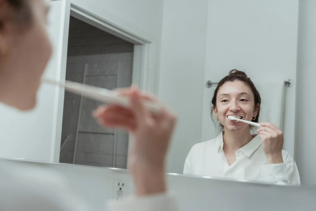 A woman with hair bun brushing her teeth in front of mirror, focusing on dental hygiene.