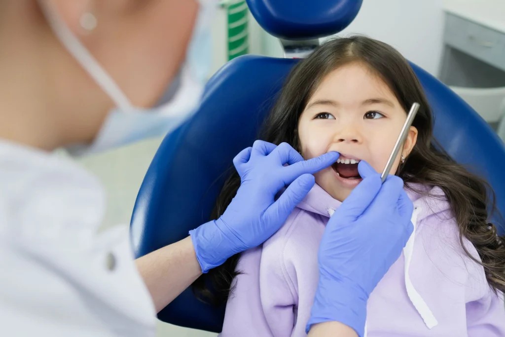 A young girl receives a dental checkup by a dentist wearing gloves in a clinic setting.
