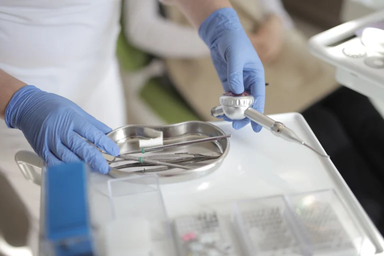 Anonymous crop doctor in latex gloves taking metal medical instruments from table while preparing for treatment in modern clinic