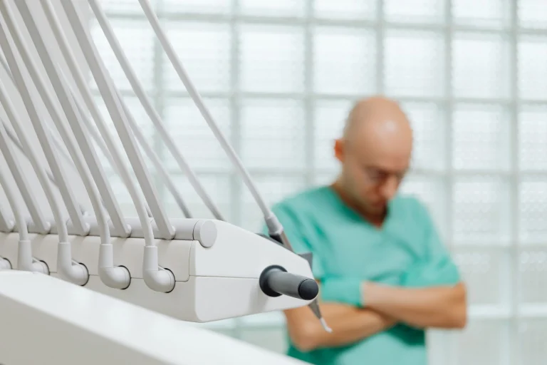 Close-up of dental tools with a blurred dentist in scrubs in the background.