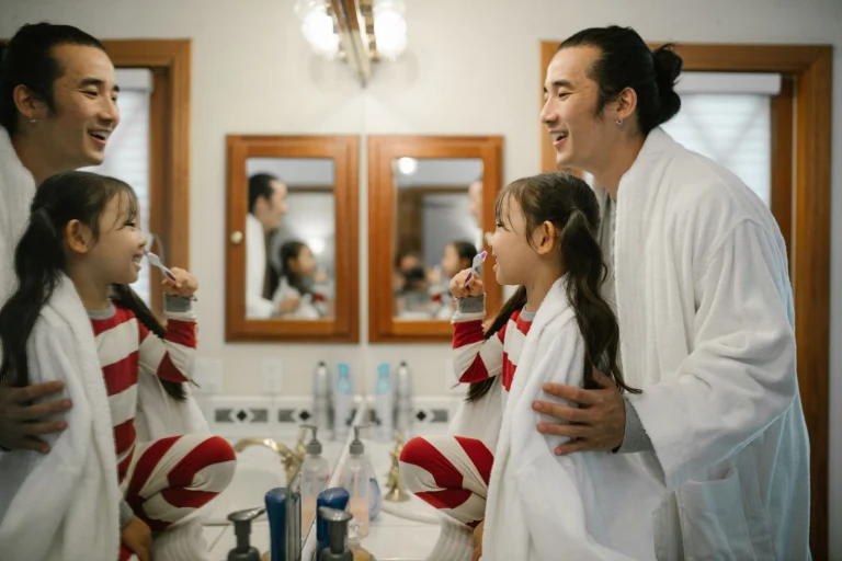 A father helps his daughter brush her teeth in a home bathroom setting, fostering good hygiene habits.
