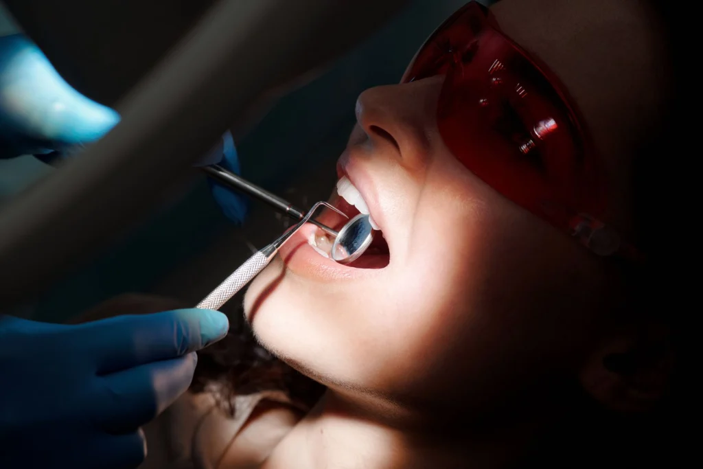 A detailed close-up of a dental examination showing tools and a patient with protective eyewear.