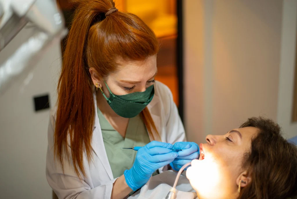 Female dentist wearing protective gear examines a patient in a dental clinic.