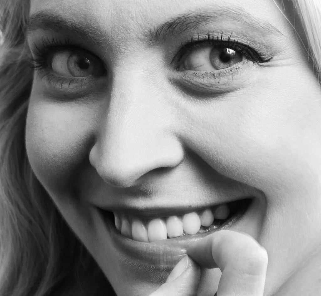 Black and white close-up portrait of a woman smiling, highlighting her eyes and white teeth.