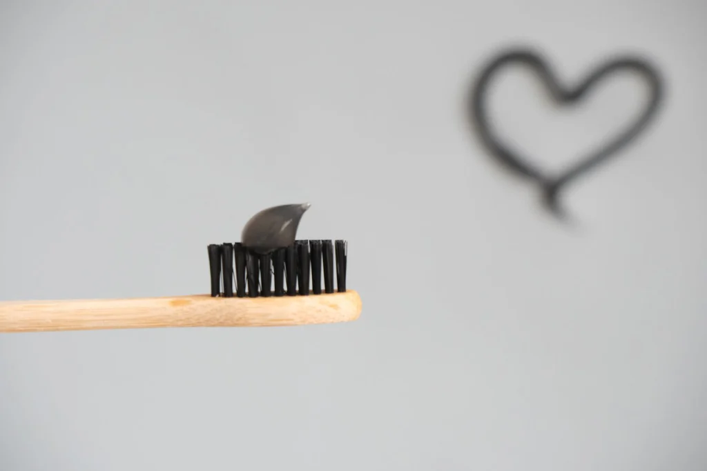 Close-up of a bamboo toothbrush with charcoal toothpaste on a neutral background.