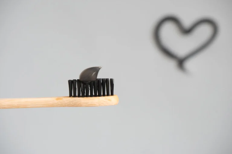Close-up of a bamboo toothbrush with charcoal toothpaste on a neutral background.