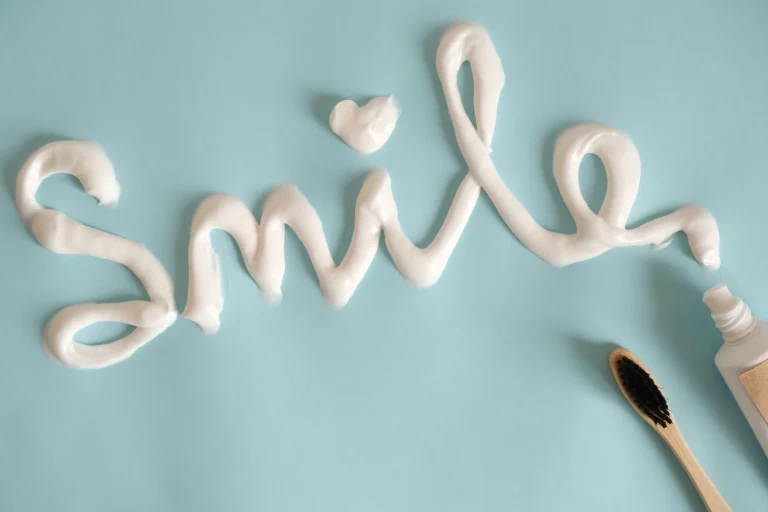 Toothpaste spelling 'Smile' on turquoise surface with toothbrush.