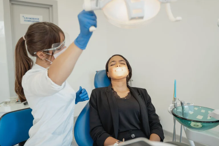 Dentist in blue gloves examines patient in black attire, illuminating dental workspace.