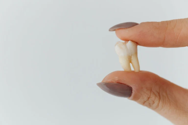 Detailed close-up of fingers holding a loose tooth against a white background.