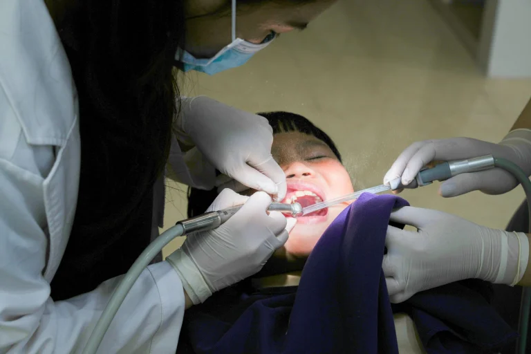 A young child receiving dental treatment from a masked dentist using dental tools indoors.