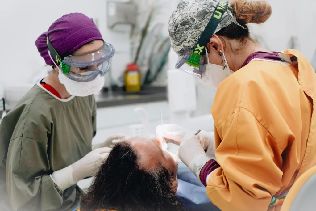 Two healthcare professionals perform a dental procedure in a medical examination room.