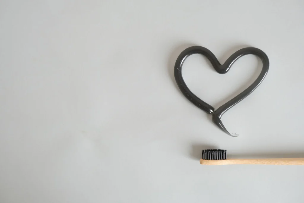 Charcoal toothpaste shaped as a heart with bamboo toothbrush on gray background. Ideal for eco-friendly dental care imagery.