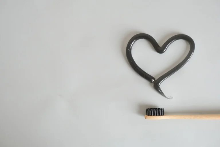 Charcoal toothpaste shaped as a heart with bamboo toothbrush on gray background. Ideal for eco-friendly dental care imagery.