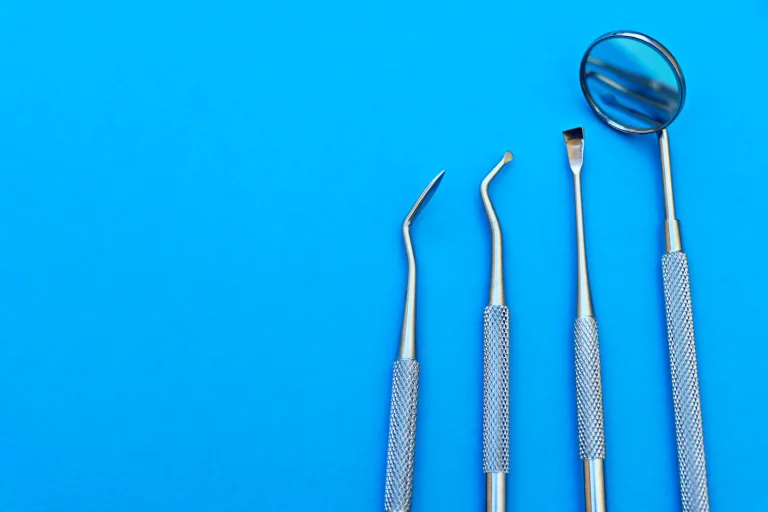 Close-up of stainless steel dental tools arranged on a bright blue surface, showcasing various instruments.