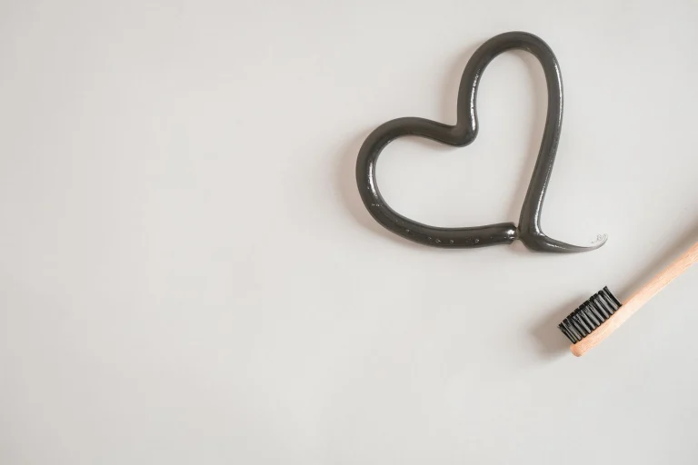 Heart shape made from charcoal toothpaste with bamboo toothbrush on white background, promoting dental care.