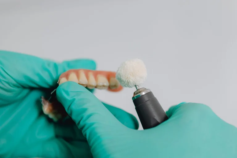 Dentist wearing gloves polishes a dental prosthetic using a specialized tool in a clinical setting.