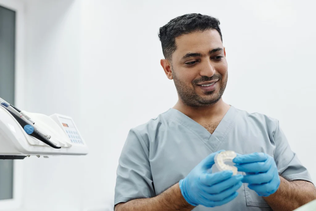 A dentist in scrubs and gloves examines a dental mold in a bright clinic setting.